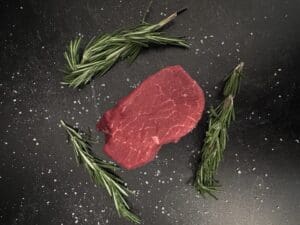 A piece of meat and some herbs on the table